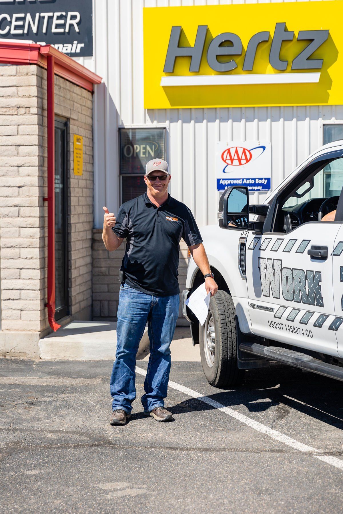 A man is standing in front of a hertz truck in a parking lot.