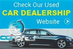 A car is parked in front of a blue sign that says `` check our used car dealership website ''.