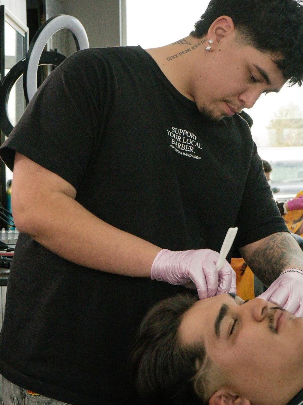 A man with a tattoo on his neck is shaving another man 's face