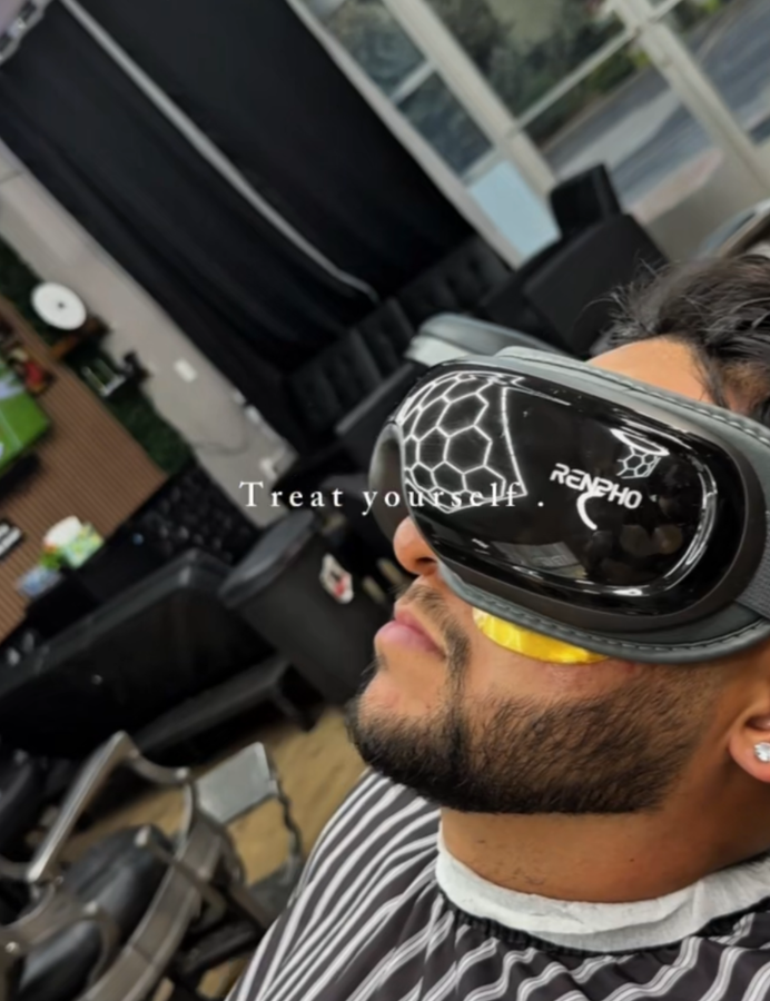 Man in barber cape getting haircut, faded hair, beard. Indoors.