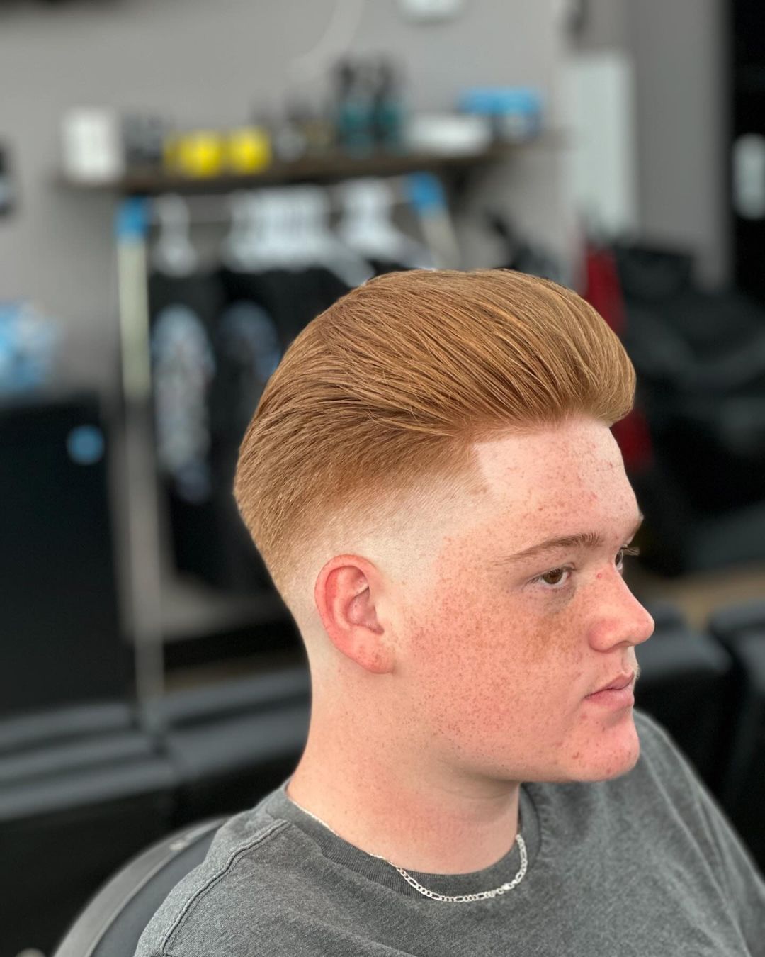 A young man with red hair is getting his hair cut at a barber shop.