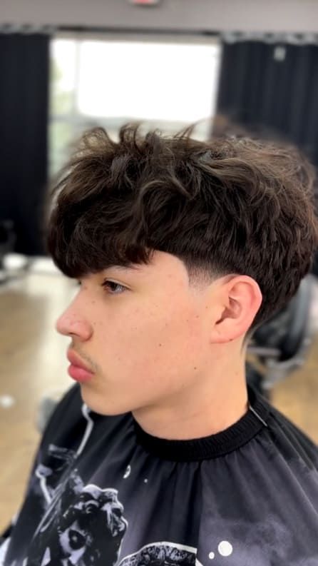 Young man with wavy brown hair, a skin fade haircut, and a serious expression.