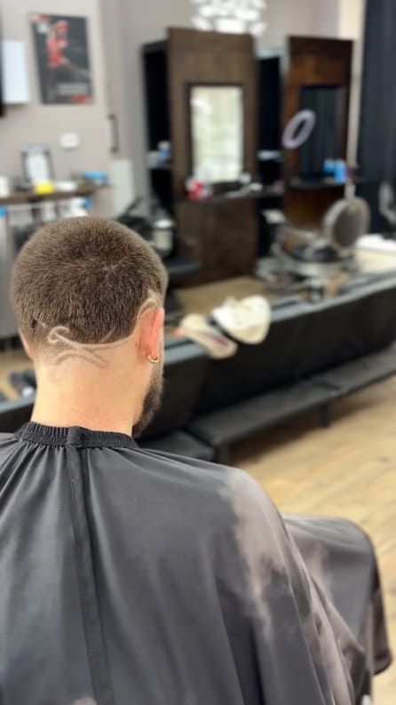 Man with short haircut at a barbershop; design shaved on the back of his head.