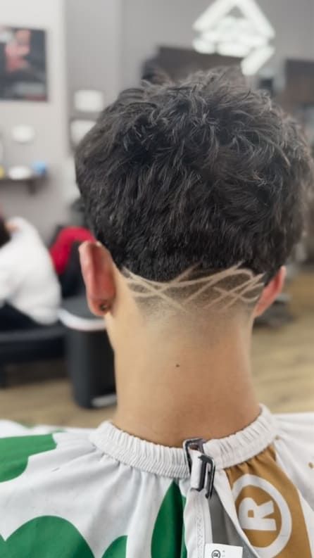 Back of person's head with dark curly hair. Faded neckline with geometric design. Barber shop setting.