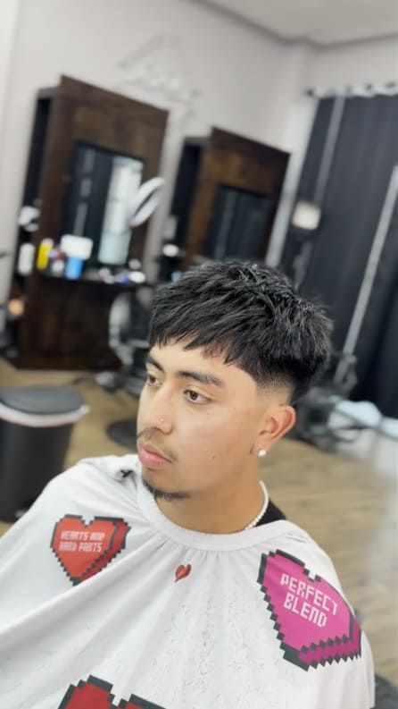 Young man with a fresh haircut in a barber shop. He wears a cape with hearts.