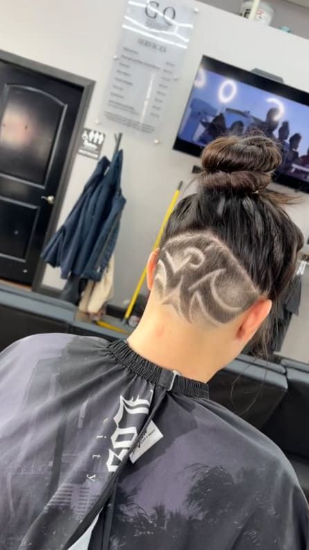 Person with a shaved head design, hair in a bun, at a barbershop.