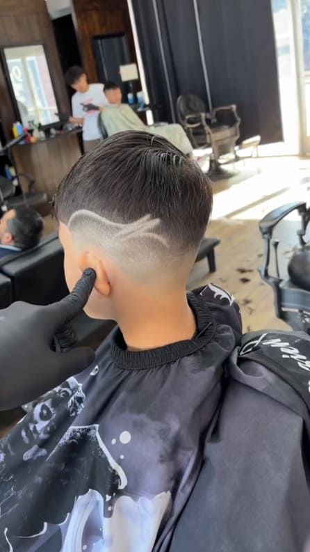 Boy getting a haircut with a design shaved into his hair at a barbershop.