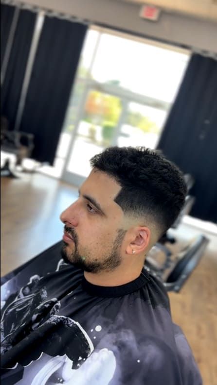Man with a fade haircut and facial hair in a barber shop setting.