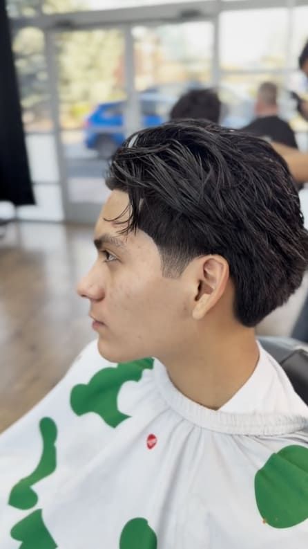 Man with dark hair, side profile, at a barber shop, wearing a green and white cape.