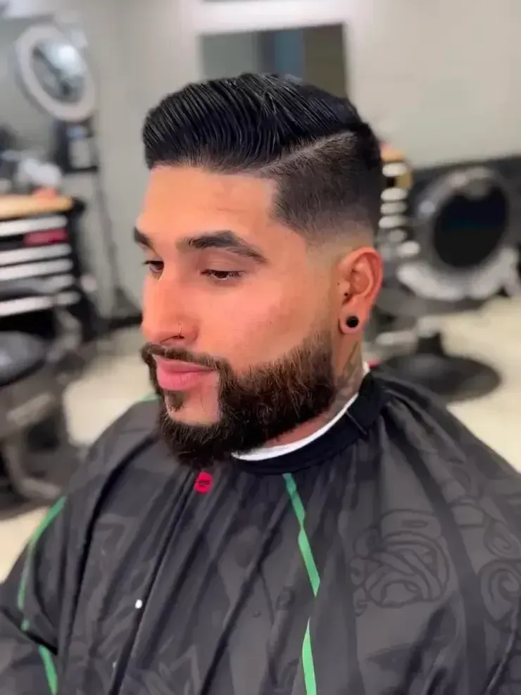 A man with a beard is getting his hair cut at a barber shop.