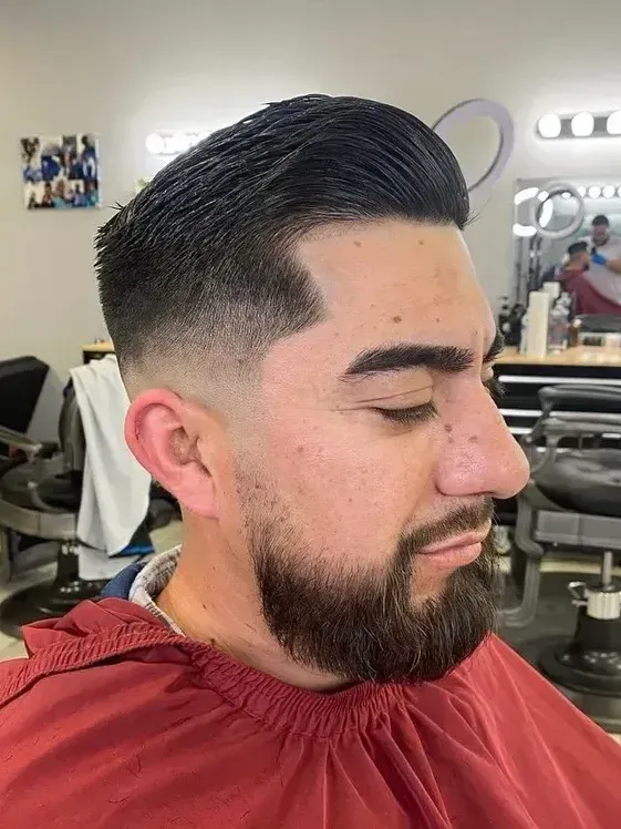 A man with a beard is getting his hair cut at a barber shop.