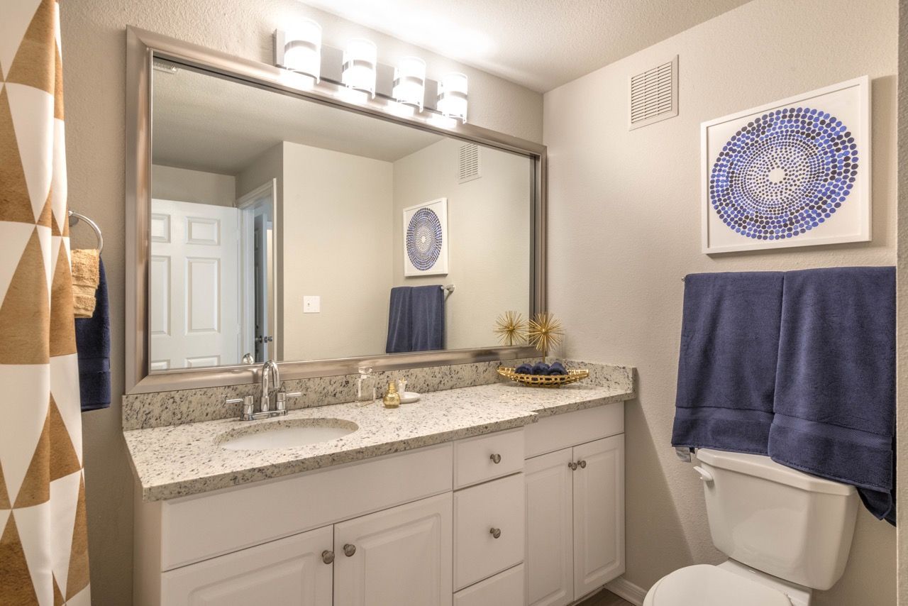 Bathroom vanity with granite countertop, large mirror, and blue towels.