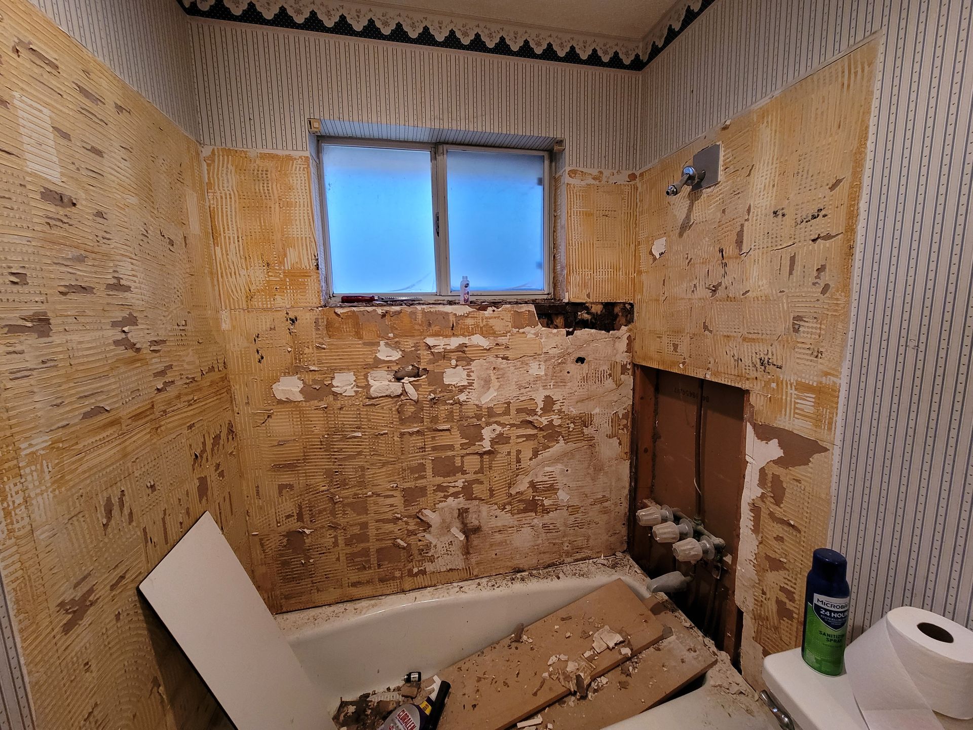 A bathroom with a tub , toilet , and window being remodeled.