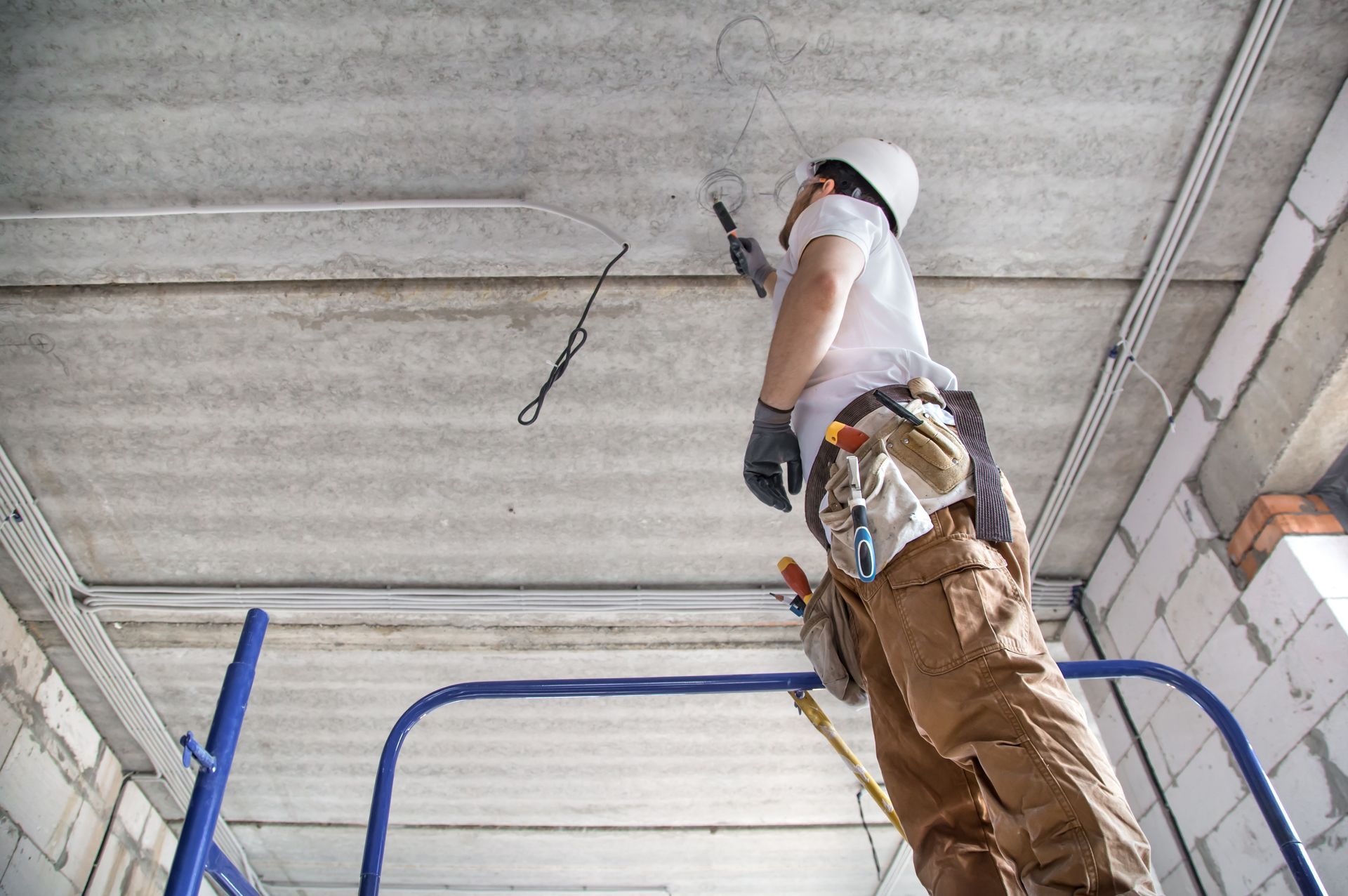 Electrician with a tool in his hands, working with a cable on a construction site.