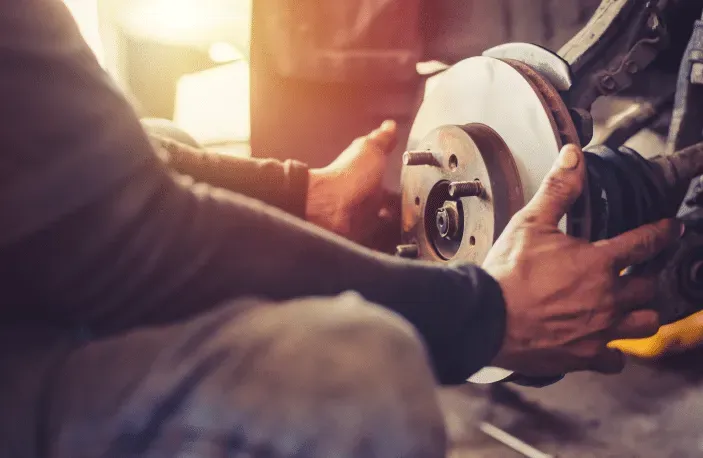 Mechanic replacing a brake rotor on a car, hands close-up. Garage setting, light, repair work.