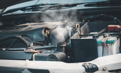 Car engine steaming. Hood open, revealing engine, battery, and steam escaping from the front.