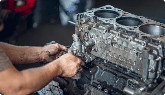Mechanic working on a car engine, likely in a garage. Hands visible, engine black and silver.