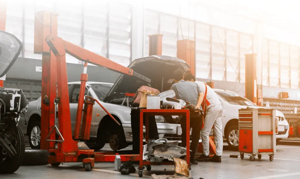 Two mechanics working on a car in a repair shop. Bright sunlight.
