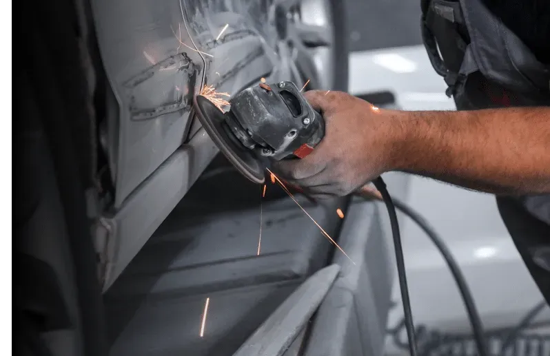 A person grinds metal on a car, sparks flying, hands visible.