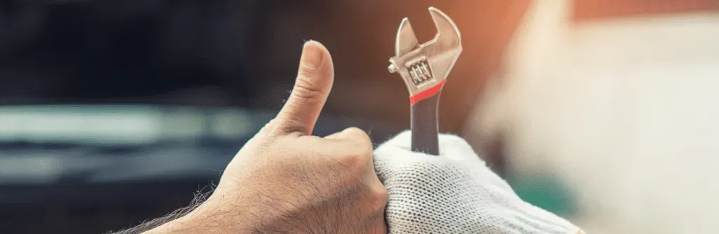 Hands holding a wrench and giving a thumbs up, likely in an auto repair shop.