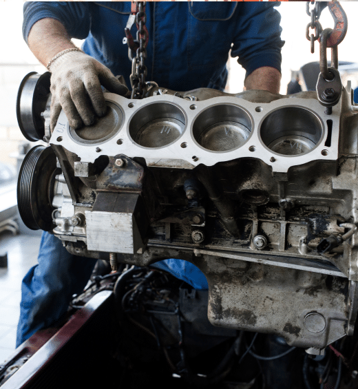 Mechanic in blue overalls working on a car engine, wearing gloves in a garage.