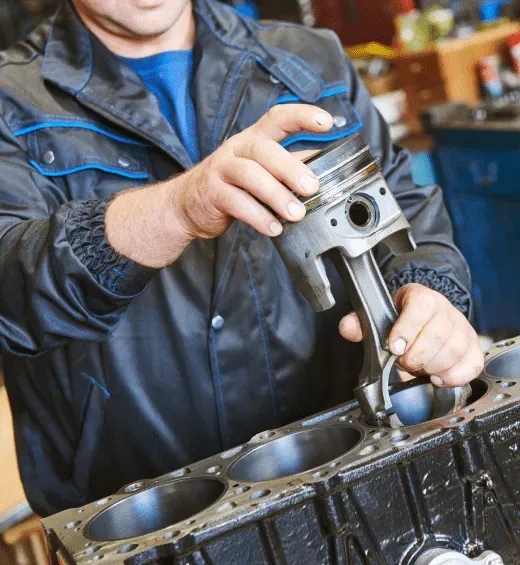 Mechanic fitting a piston into an engine block in a garage setting.