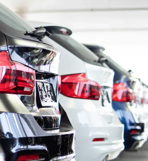 Rear view of several modern cars parked in a row; black, white, and blue vehicles are visible.