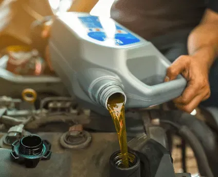 Person pouring motor oil from a gray container into a car engine.