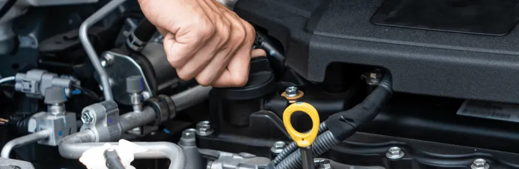 A hand is working on a car engine with tools and tubes visible.