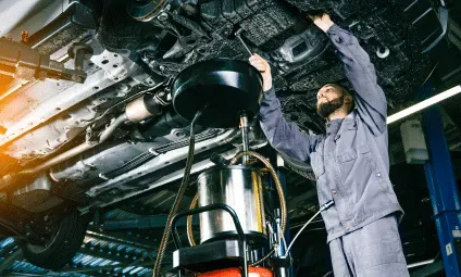 Mechanic changing oil under a car in a garage.