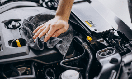 Hand wiping down a car engine with a gray cloth.