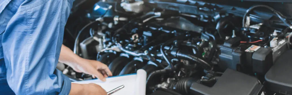 Mechanic in blue shirt, inspecting car engine, holding checklist.