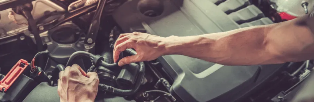 Person working on a car engine, hands visible.