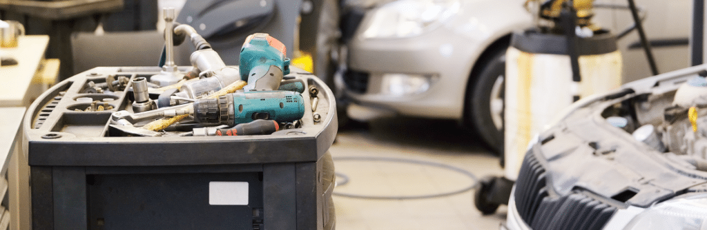 A mechanic's workspace with tools, a drill, and a car being worked on.