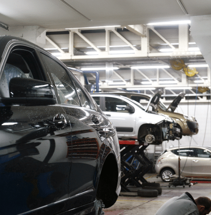 Cars in a repair shop; one black car close-up, others on lifts, mechanic working.