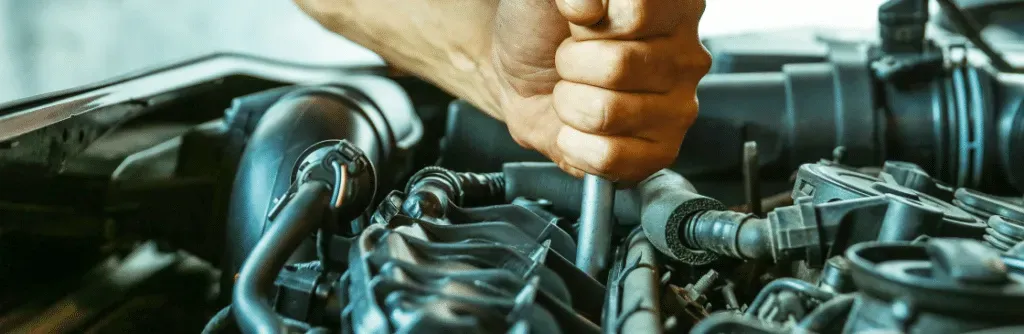 A hand working on a car engine with a wrench.