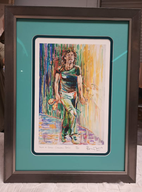 Framed print of Mick Jagger in colorful alleyway. He's holding dolls, walking towards light.