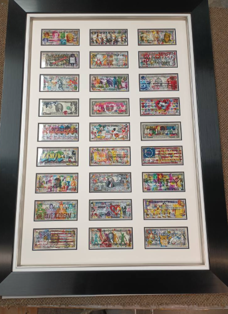 Framed artwork of colorful, painted US dollar bills arranged in rows. Black frame with white mat.
