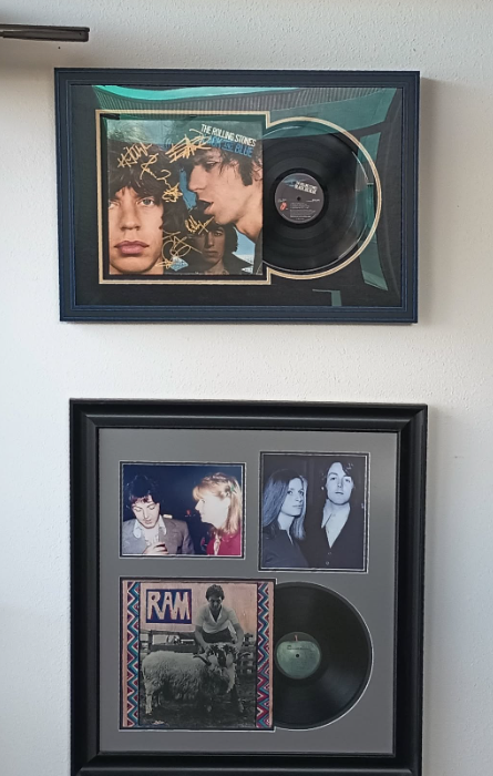 Two framed records and images, one with a blue and brown album cover, the other with a green album cover and photos.