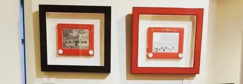 Two red Etch-a-Sketch toys, framed in black and red, hung on a white wall.