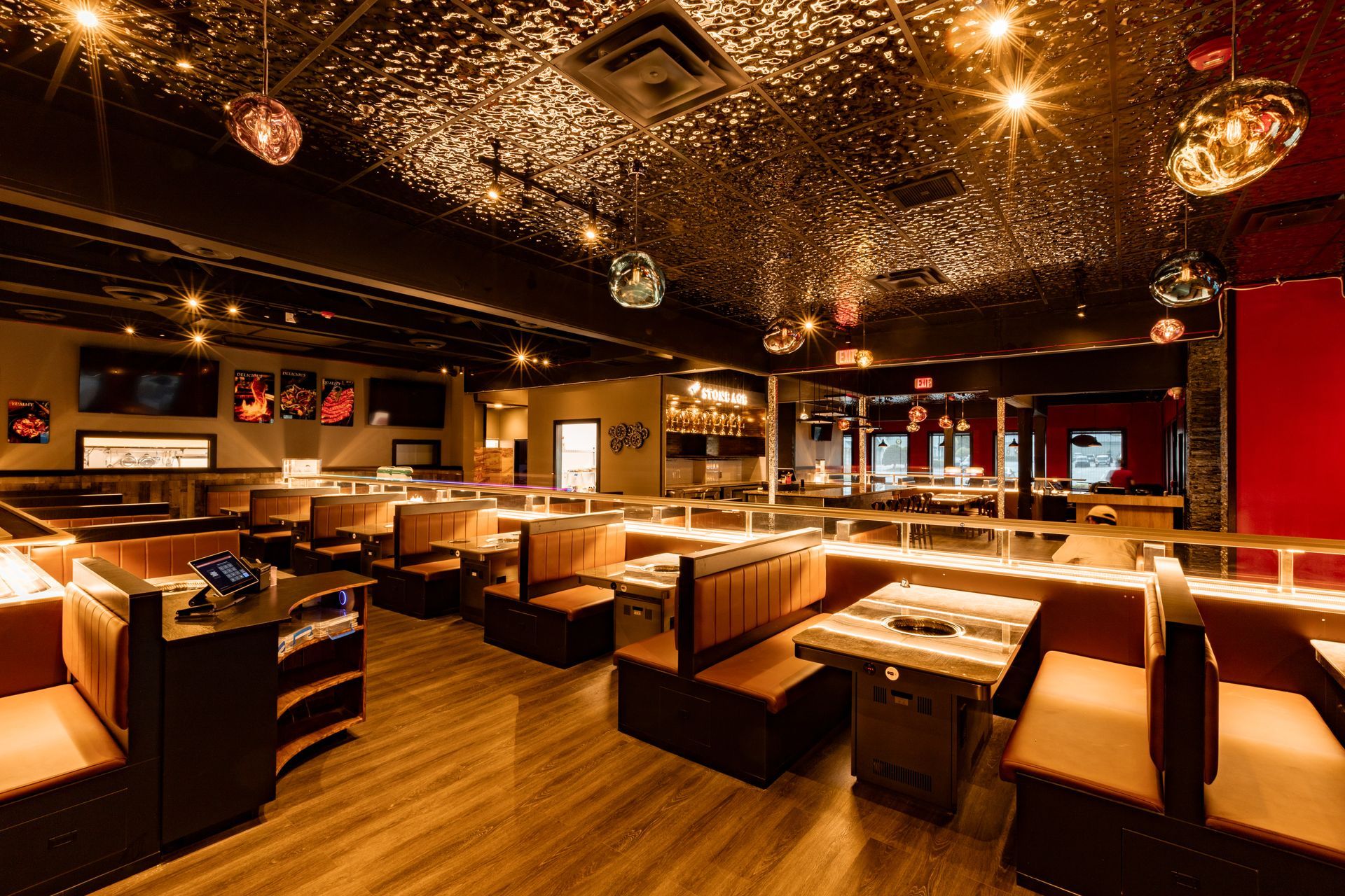 Interior of a restaurant with booths and tables, wooden floor, and metallic ceiling. Lights hang throughout.