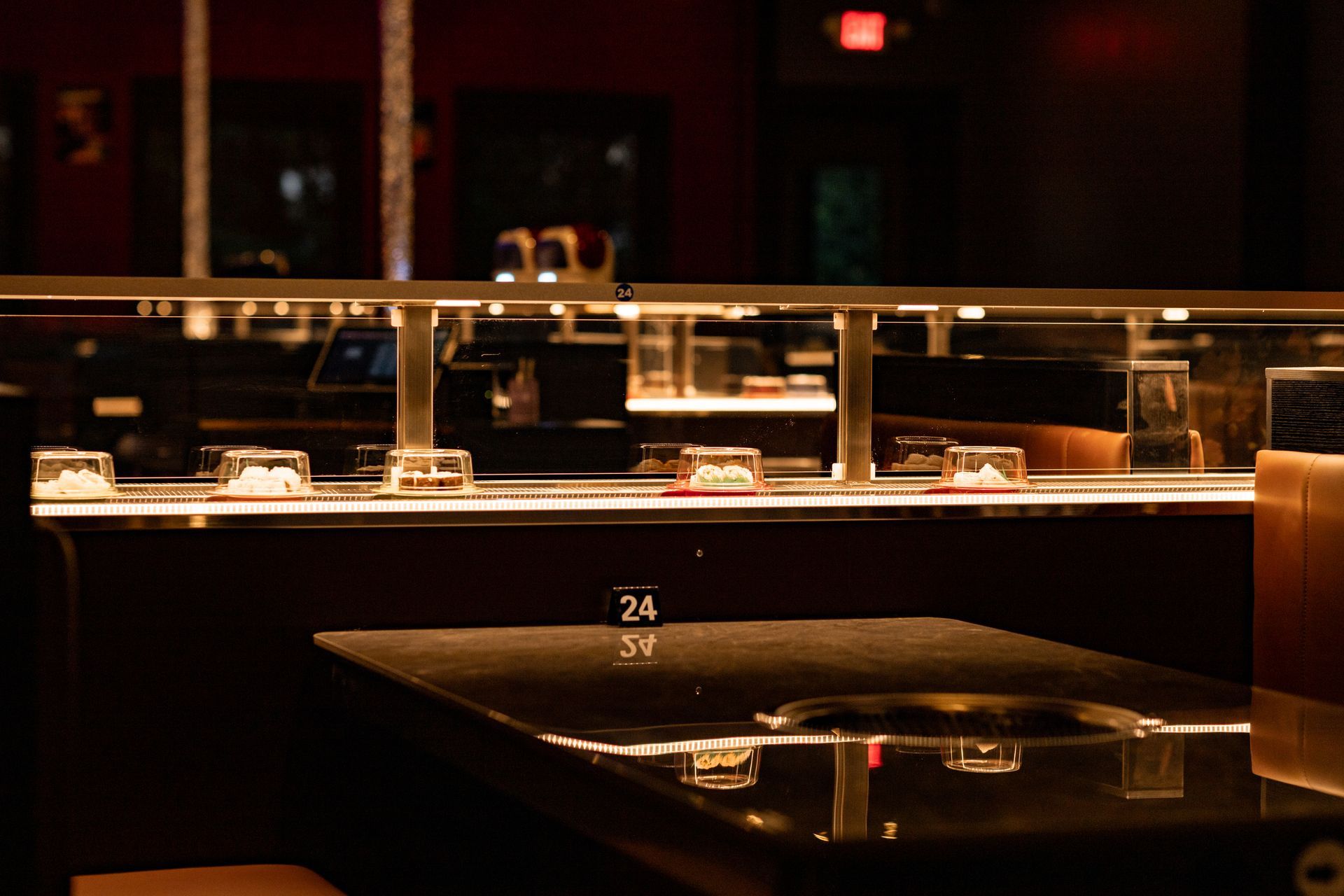 Sushi bar interior with a conveyor belt carrying small dishes past a black table. Dark, upscale setting.