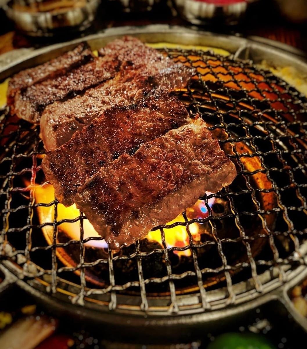 Grilled beef slices on a metal grate over flames, likely at a Korean barbecue restaurant.