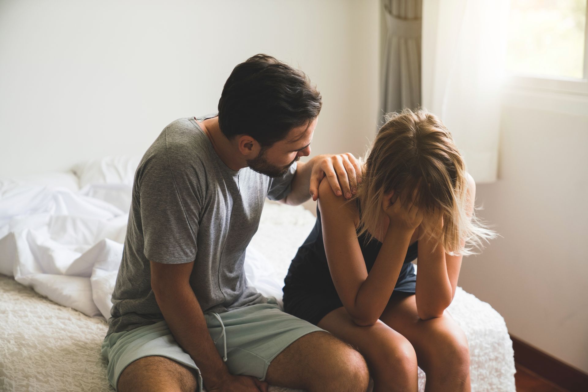A man is comforting a woman who is crying while sitting on a bed.