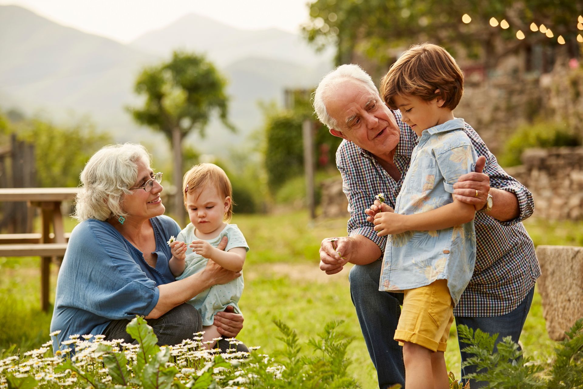 An elderly couple is holding two children while sitting in a garden.