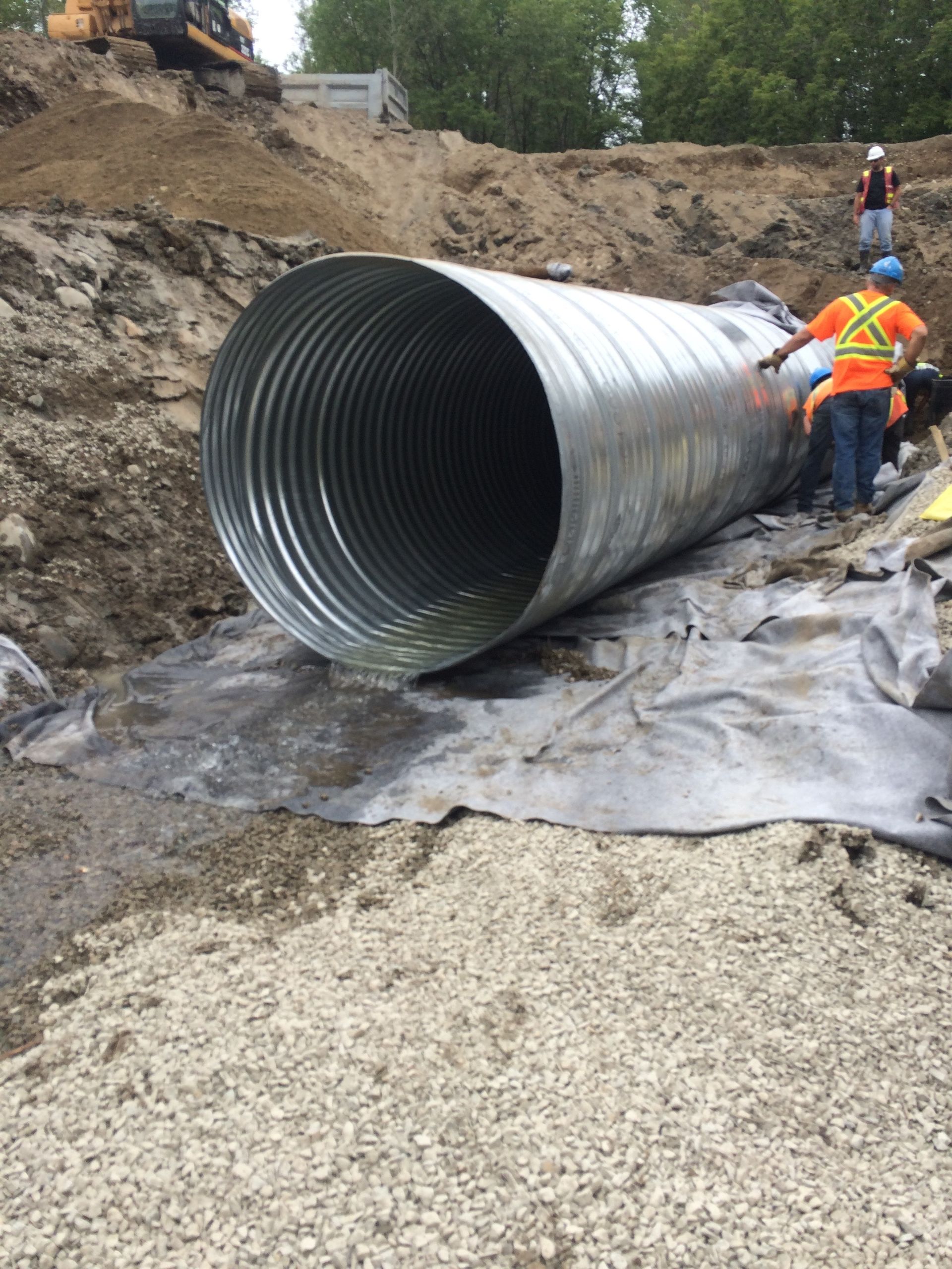 Un gros tuyau métallique repose sur un tas de gravier.