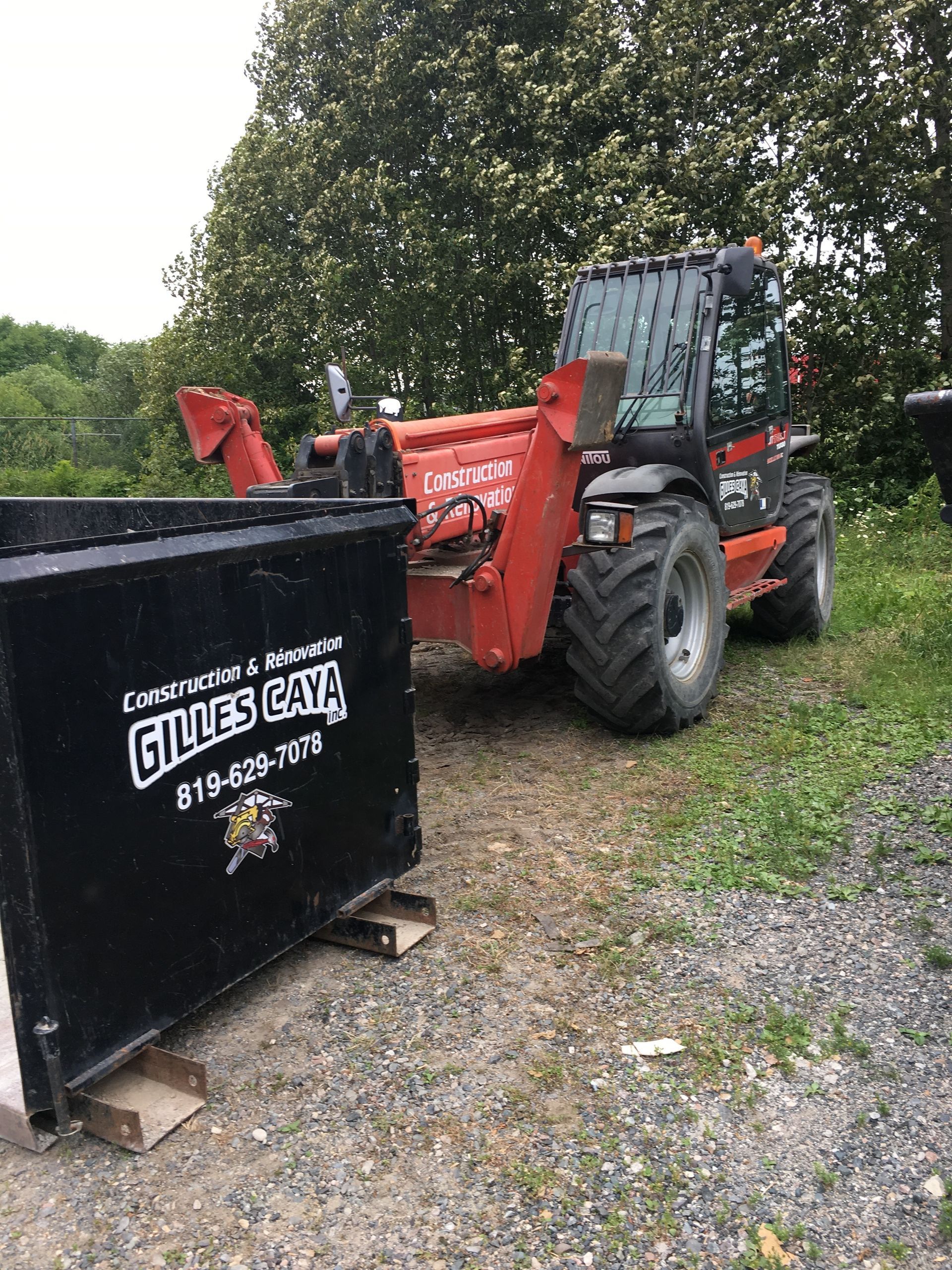 Un chariot élévateur rouge est garé à côté d’une benne noire dans un terrain de gravier.