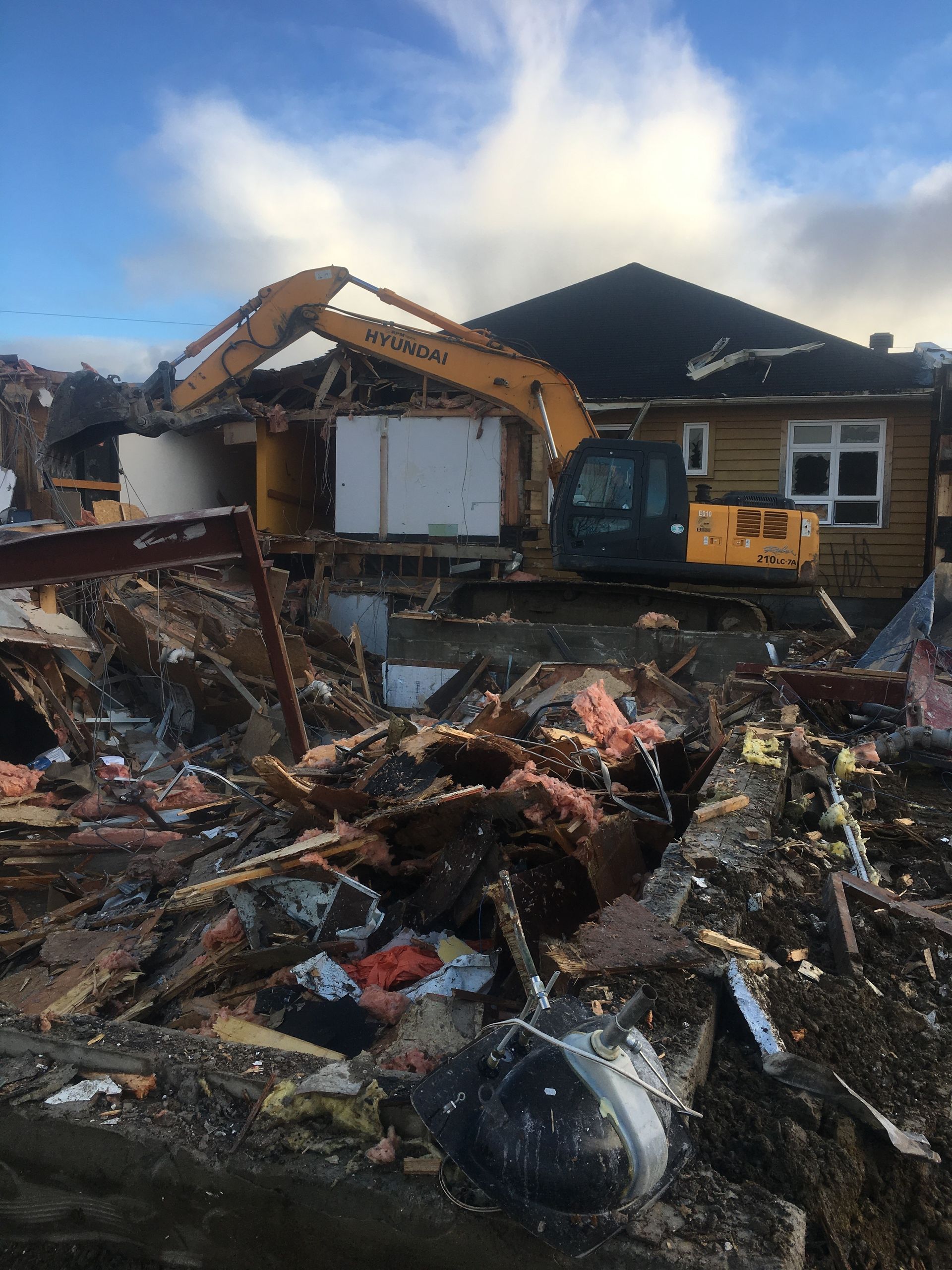Une grande excavatrice jaune est en train de démolir une maison.
