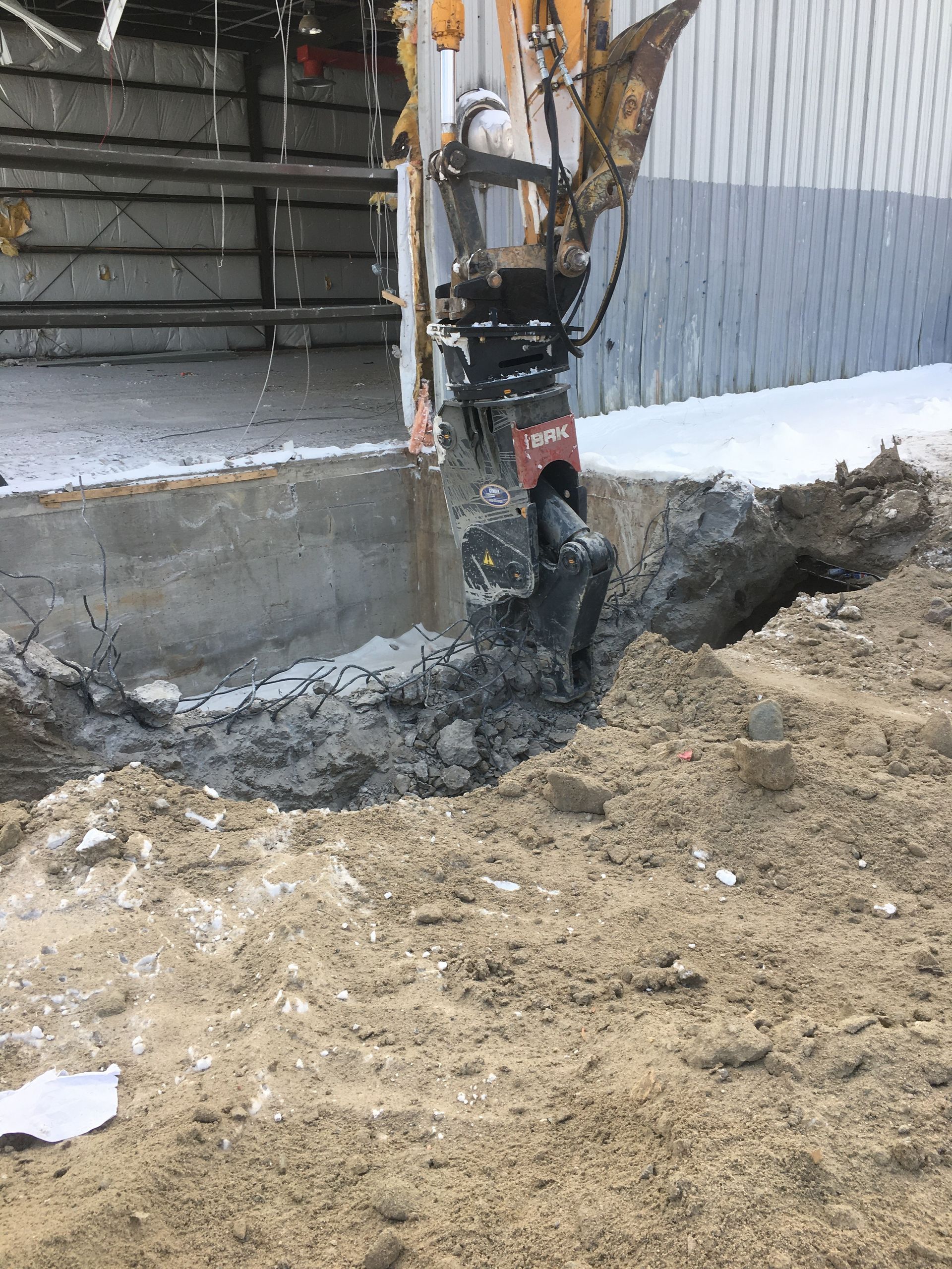 Une excavatrice creuse un trou dans le sol devant un bâtiment.