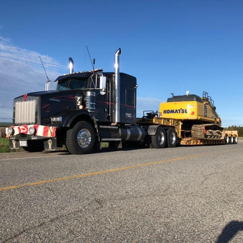 Un camion Komatsu tire une pelle jaune sur une remorque